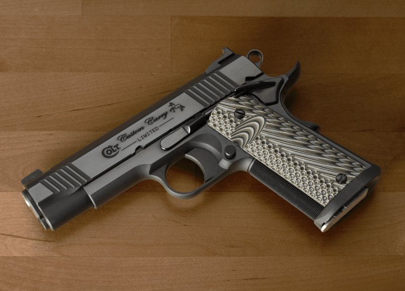 Side view of a semi-automatic handgun with textured grip panels on a wooden surface.